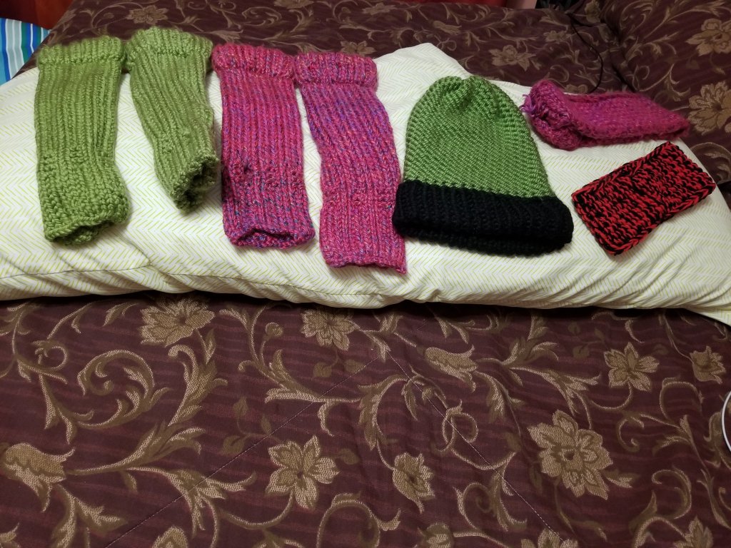 2 sets of long fingerless gloves 1 is green 1 is a purple burgundy  color. There is a green hat with a black brim. There are 2 ear warmers 1 is purple burgundy  and the other is black and red.