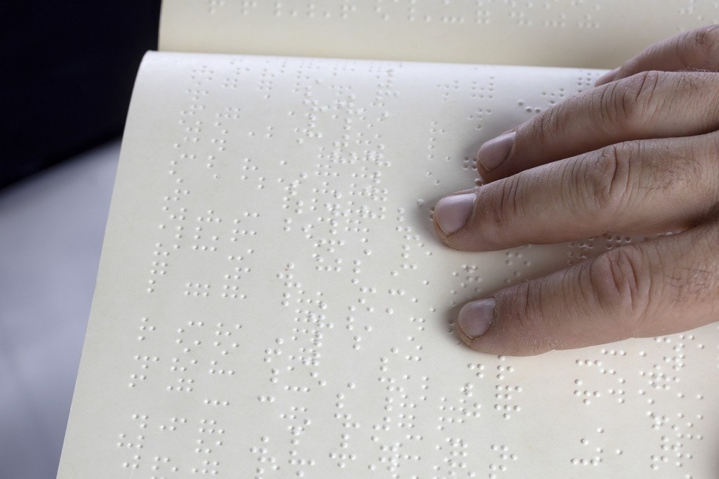 Image shows fingers on a page as a person reads braille.