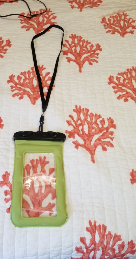 A photo of my plastic waterproof phone case. The case has a strap to secure it over your head. The case is on a background that has pink and coral colors. 
#summer #phones #phonecases #summeressentials 