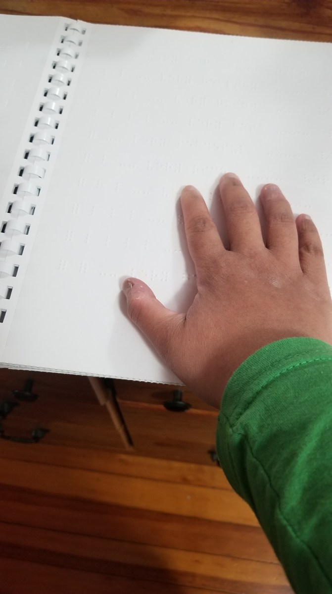 A hand reading braille on a page