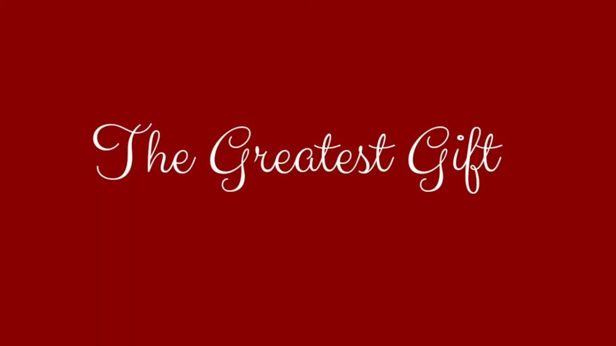 The image has a solid red background with the words "The Greatest Gift" written in the center in white, elegant, cursive font.